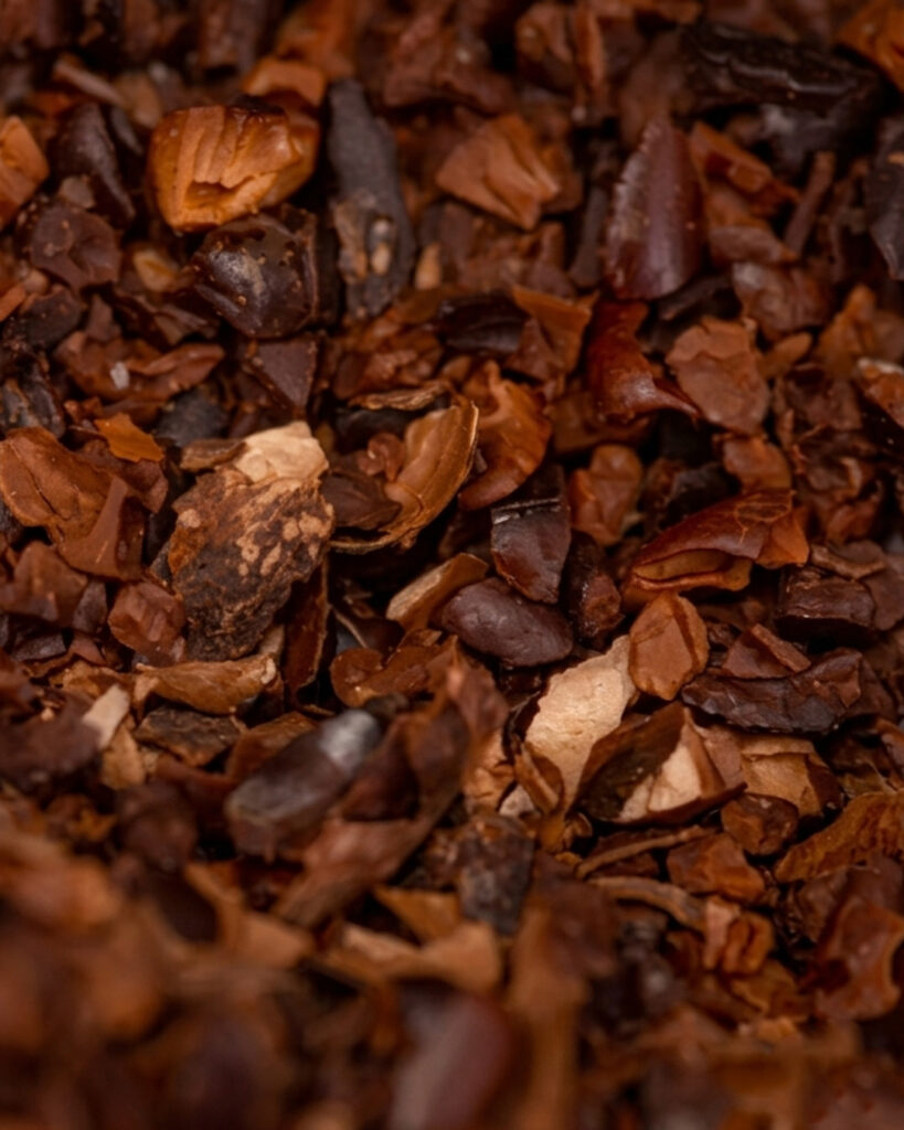 A dense, close-up pile of dry, dark brown and reddish cocoa bean husks with a papery, curved texture.